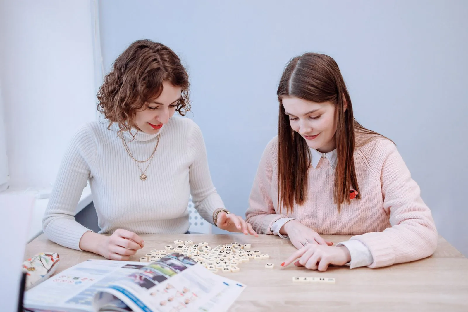 Friends playing Scrabble together on a wooden table, enjoying leisure time indoors.